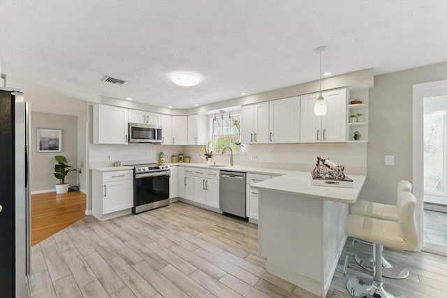 kitchen with stainless steel appliances, a peninsula, white cabinets, light countertops, and recessed lighting