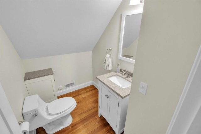 half bath with visible vents, lofted ceiling, toilet, wood finished floors, and vanity