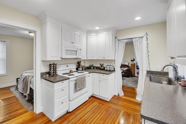 kitchen featuring dark countertops, white appliances, white cabinets, and a sink