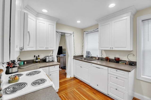 kitchen with dark countertops, white dishwasher, a sink, and white cabinetry