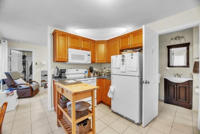 kitchen with white appliances, brown cabinetry, dark countertops, a sink, and light tile patterned flooring