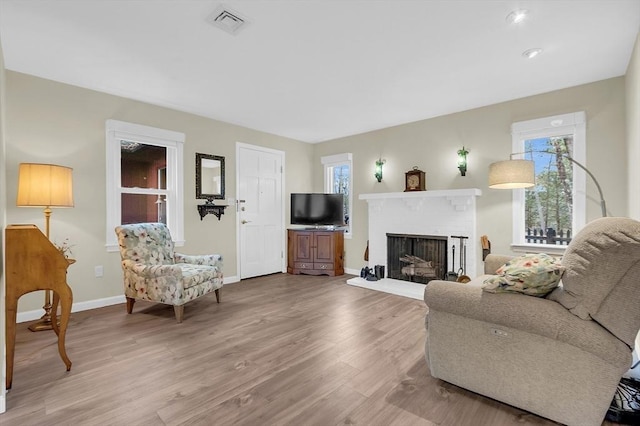 living room featuring wood-type flooring, a brick fireplace, and a wealth of natural light