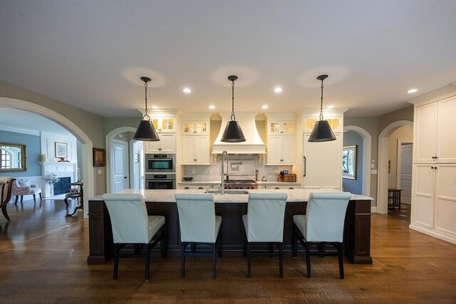 5 Copperbeech Cir, Westborough, MA 01581 - kitchen with custom exhaust hood, arched walkways, decorative backsplash, white cabinetry, and a breakfast bar area