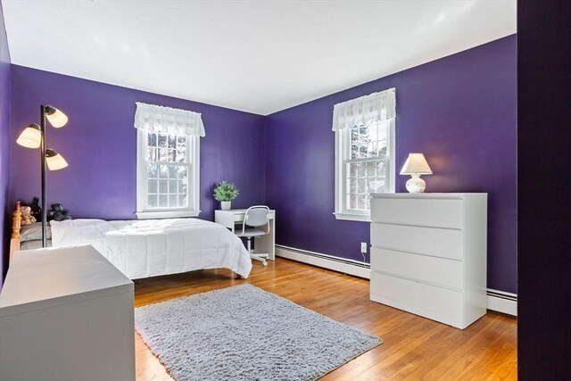 bedroom with a baseboard heating unit and light wood-style floors