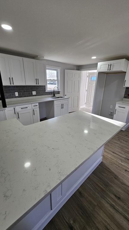 kitchen with light stone counters, dark wood-type flooring, and white cabinets