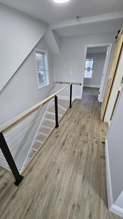 hallway featuring light wood-type flooring, a barn door, and lofted ceiling