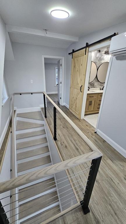 staircase featuring an AC wall unit, wood-type flooring, beam ceiling, and a barn door