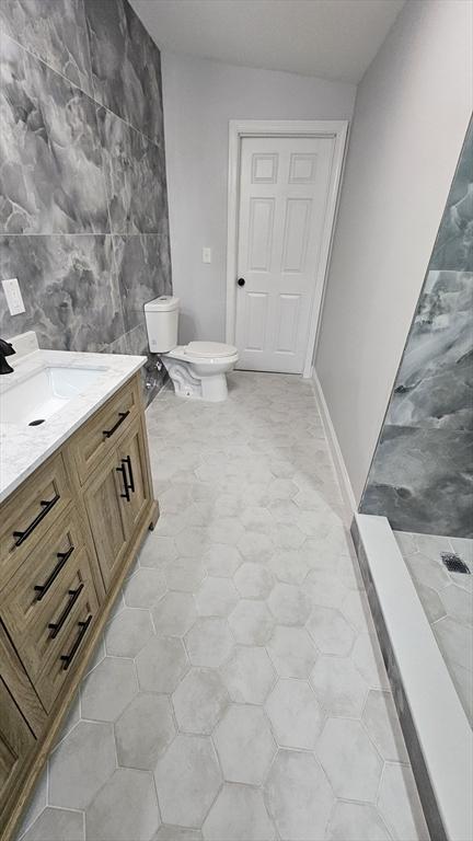 bathroom featuring tile walls, toilet, walk in shower, vanity, and lofted ceiling