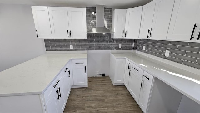 kitchen with dark wood-type flooring, white cabinetry, wall chimney range hood, tasteful backsplash, and light stone counters