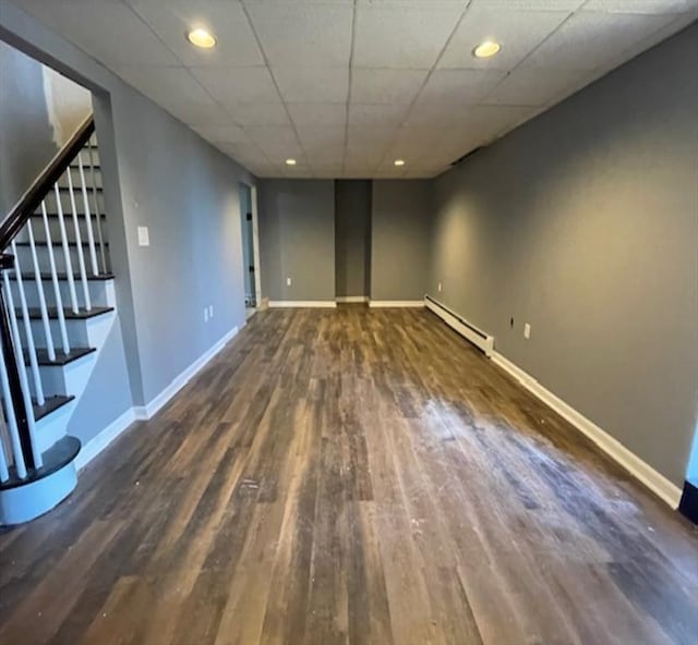 basement featuring dark hardwood / wood-style flooring, baseboard heating, and a paneled ceiling