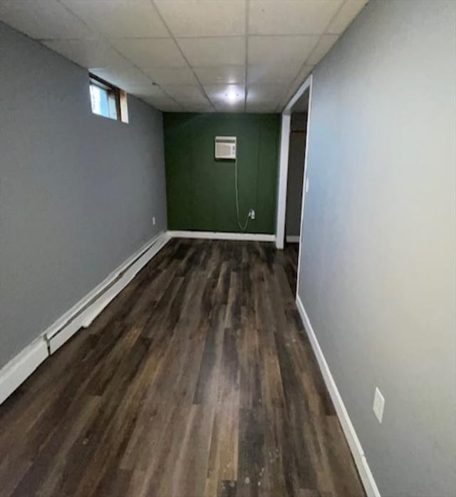 basement with dark hardwood / wood-style flooring, a wall unit AC, and a paneled ceiling