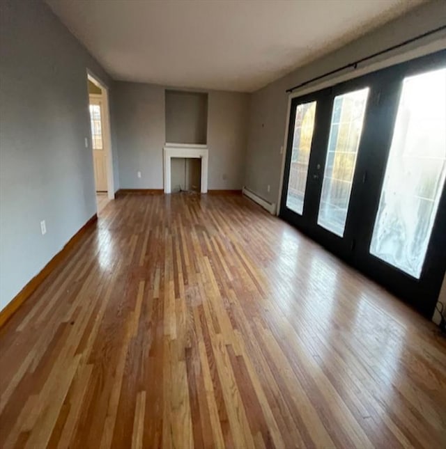 unfurnished living room with a baseboard heating unit, wood-type flooring, and french doors