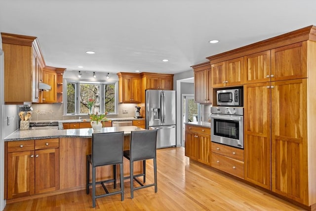 kitchen featuring a peninsula, appliances with stainless steel finishes, decorative backsplash, and light wood-style floors