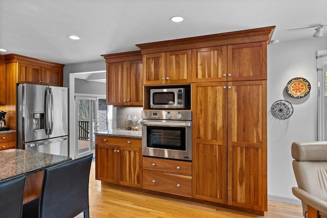 kitchen with light wood-style floors, recessed lighting, stainless steel appliances, and dark stone countertops