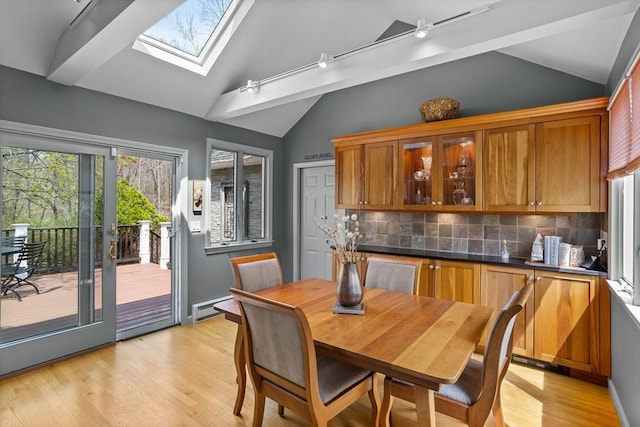 dining space with track lighting, baseboards, lofted ceiling with skylight, a baseboard radiator, and light wood finished floors