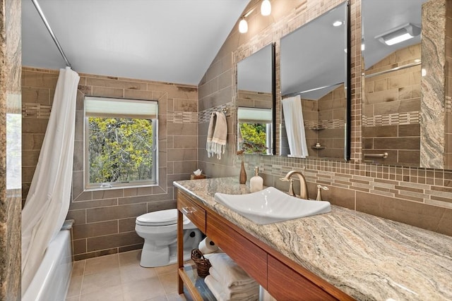 bathroom with tile walls, tile patterned floors, vanity, toilet, and lofted ceiling
