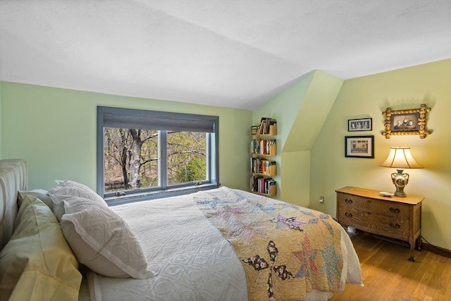 bedroom featuring baseboards, wood finished floors, and lofted ceiling