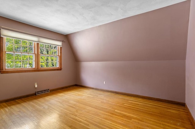 additional living space with baseboards, visible vents, light wood-type flooring, and lofted ceiling