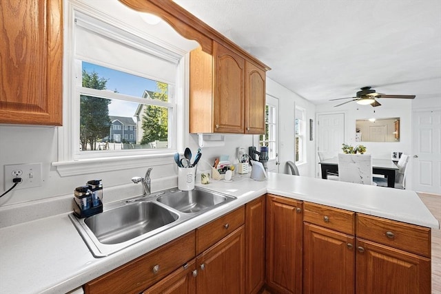 kitchen featuring a peninsula, a ceiling fan, brown cabinetry, and a sink