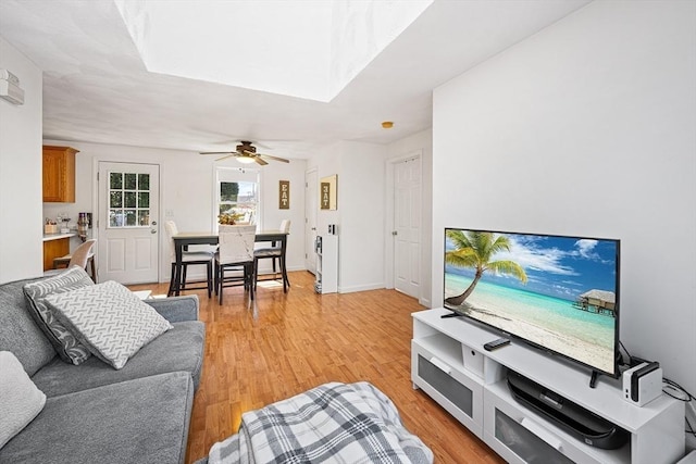 living area featuring a skylight, a ceiling fan, and light wood-style flooring