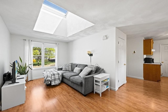 living room featuring a skylight, baseboards, and light wood-type flooring