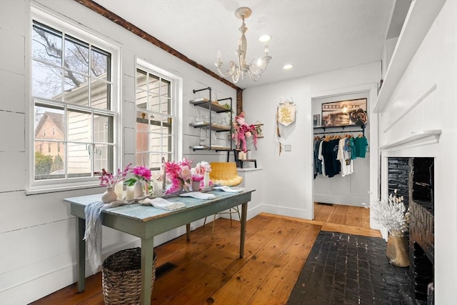 dining space with a healthy amount of sunlight, a notable chandelier, a stone fireplace, and wood-type flooring