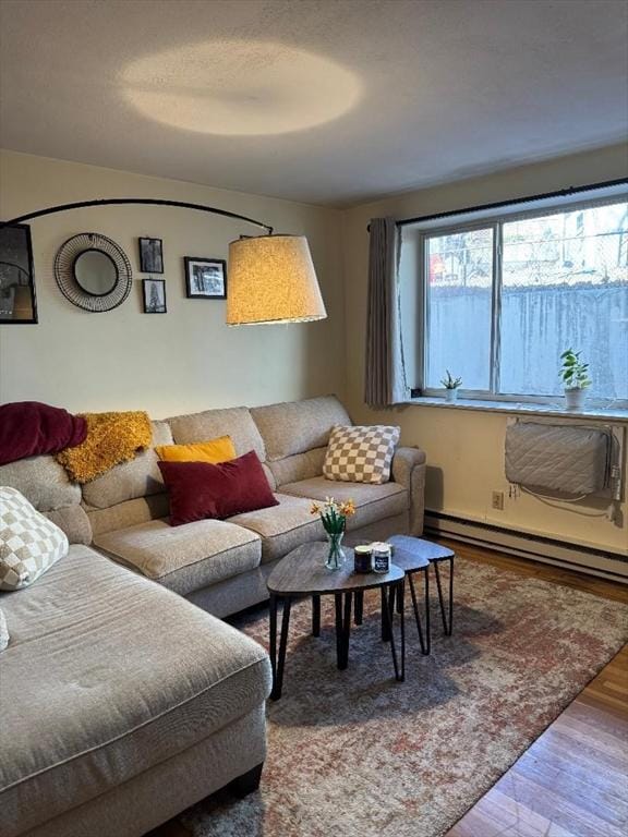 living area with a baseboard heating unit, a wall unit AC, wood finished floors, and a wealth of natural light