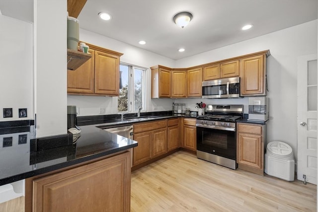 kitchen with sink, dark stone countertops, kitchen peninsula, stainless steel appliances, and light hardwood / wood-style flooring