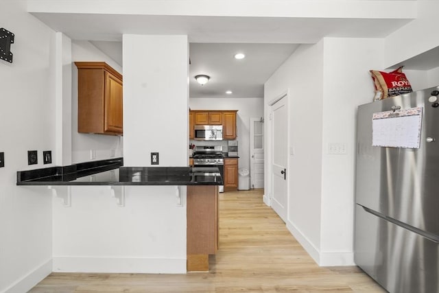 kitchen featuring stainless steel appliances, a kitchen breakfast bar, kitchen peninsula, and light wood-type flooring