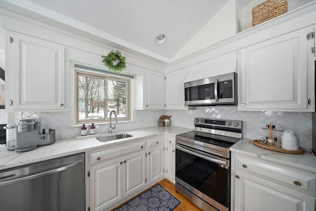 kitchen featuring light stone counters, appliances with stainless steel finishes, white cabinets, vaulted ceiling, and a sink