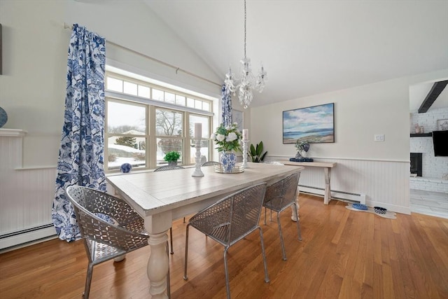 dining area with lofted ceiling, a baseboard heating unit, wood finished floors, and wainscoting