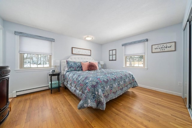 bedroom featuring a baseboard heating unit, baseboards, and light wood finished floors