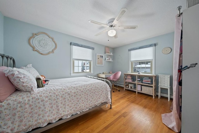 bedroom with light wood-type flooring, a baseboard radiator, and a ceiling fan