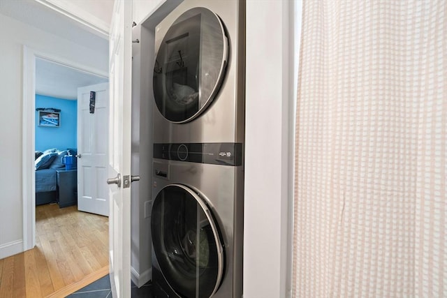 laundry room featuring laundry area, stacked washer / dryer, wood finished floors, and baseboards