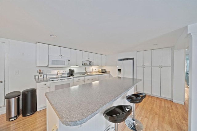 kitchen with a center island, light wood-style flooring, white cabinets, white appliances, and a kitchen breakfast bar