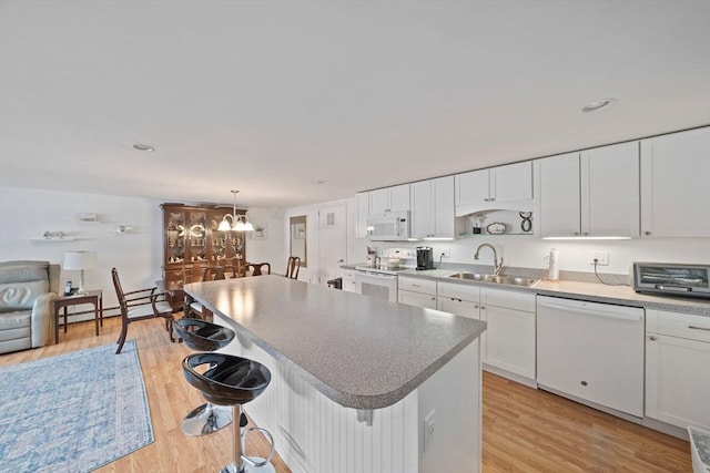 kitchen with decorative light fixtures, white cabinets, a sink, white appliances, and a kitchen bar