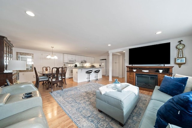 living area featuring recessed lighting, light wood-type flooring, a glass covered fireplace, and an inviting chandelier