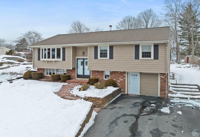 raised ranch with a garage, aphalt driveway, and brick siding