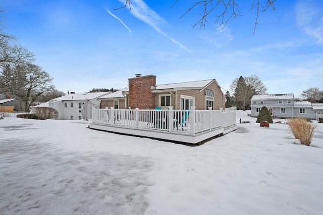 snow covered back of property with a chimney and a deck