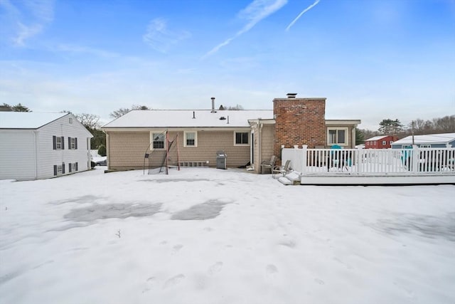 snow covered back of property with a chimney and fence