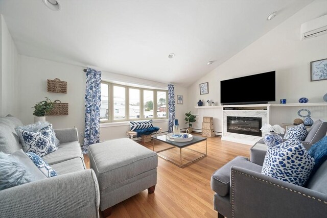 living area featuring lofted ceiling, a wall unit AC, recessed lighting, wood finished floors, and a high end fireplace