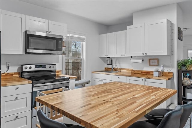 kitchen with butcher block counters, white cabinetry, and appliances with stainless steel finishes