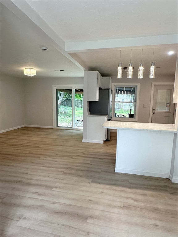 kitchen featuring light wood-type flooring, pendant lighting, white cabinetry, beam ceiling, and kitchen peninsula