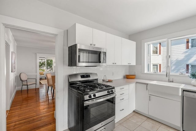 kitchen featuring sink, backsplash, light tile patterned floors, appliances with stainless steel finishes, and white cabinets