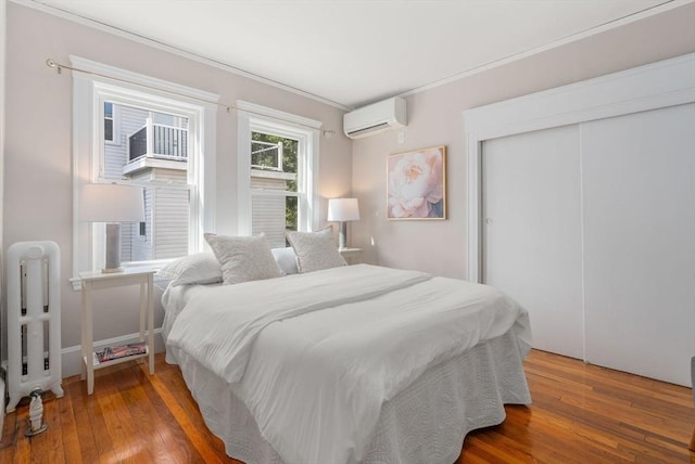 bedroom with radiator heating unit, wood-type flooring, a closet, and a wall mounted air conditioner