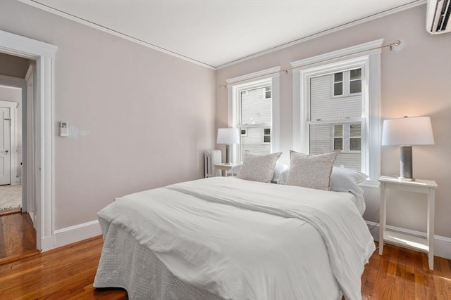 bedroom featuring hardwood / wood-style flooring, a wall unit AC, and ornamental molding