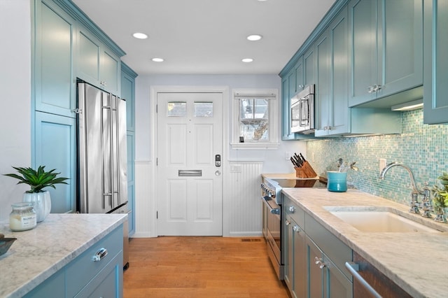 kitchen featuring stainless steel appliances, sink, light stone counters, and light hardwood / wood-style flooring