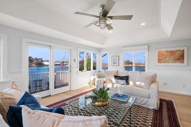 living room featuring a tray ceiling, a water view, and light hardwood / wood-style floors