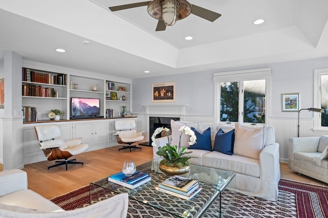 living room with hardwood / wood-style floors, ceiling fan, a raised ceiling, and built in shelves