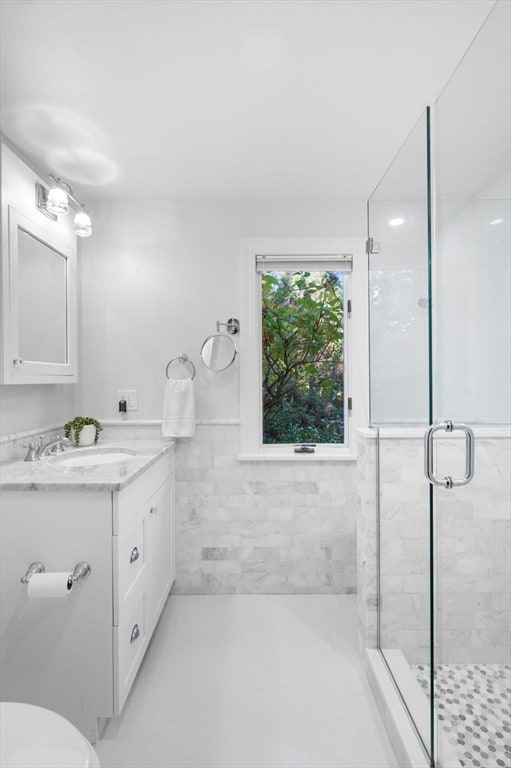 bathroom with tile walls, vanity, toilet, and a shower with door